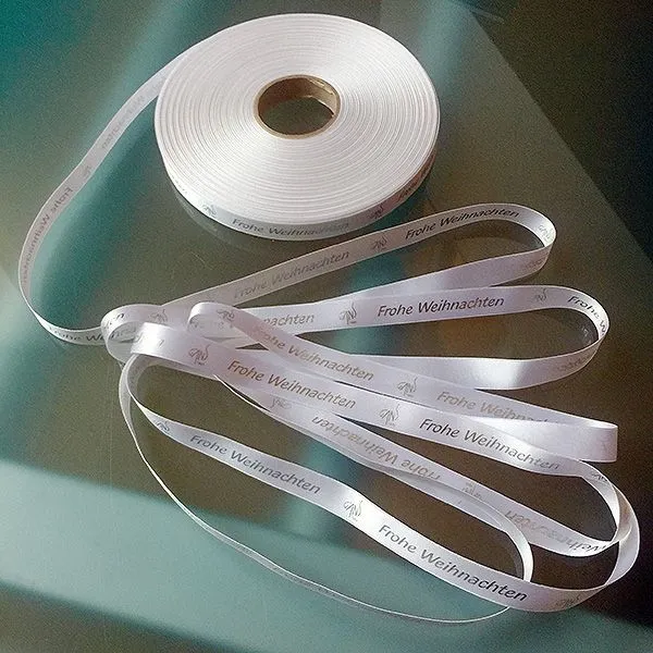 Produktbild von Satin-Geschenkband mit individuellem Foliendruck in Silber auf 50-m-Rollen, 16 mm breit, aus 100% Polyester, weiß.